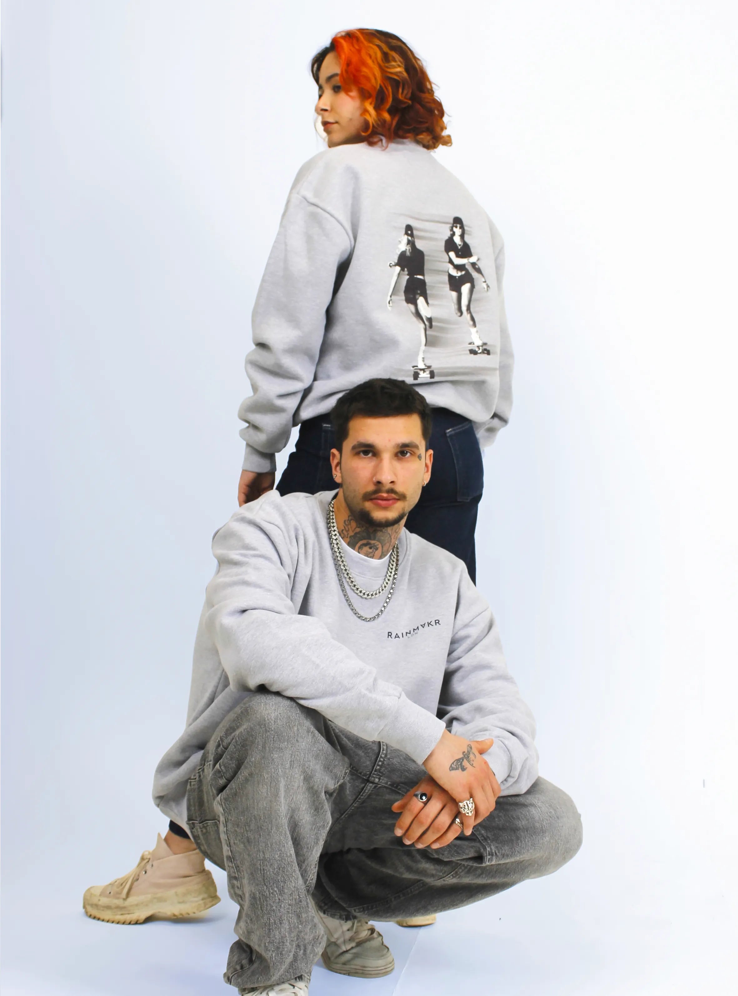 Two models wearing grey crewneck sweatshirts with a skater print design at the back. One male and one female.